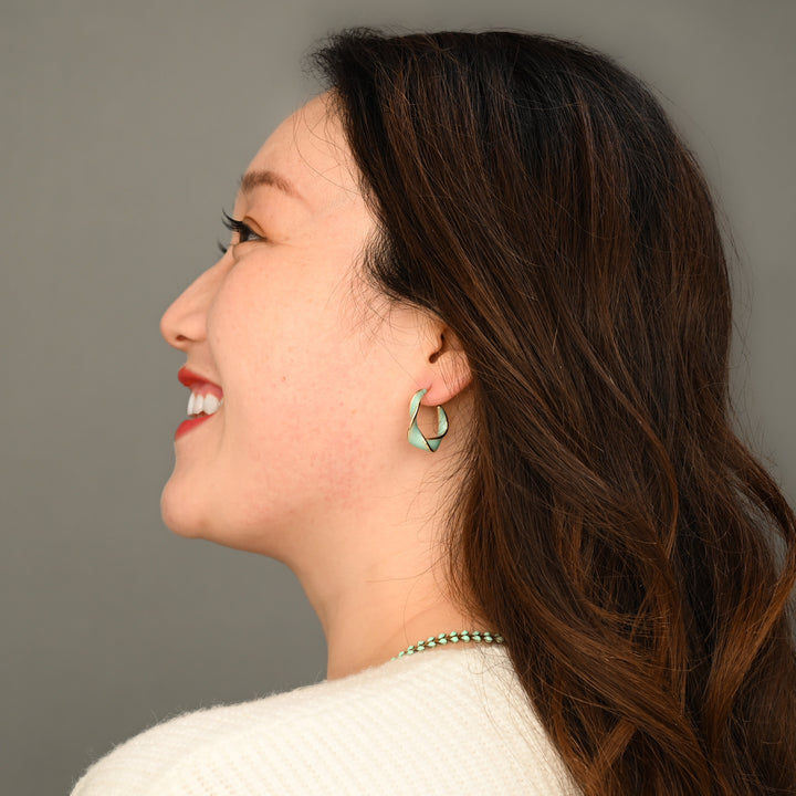 A woman wearing gold plated mint green hoops, green hoop earrings, twist shape hoops, jewellery stores online