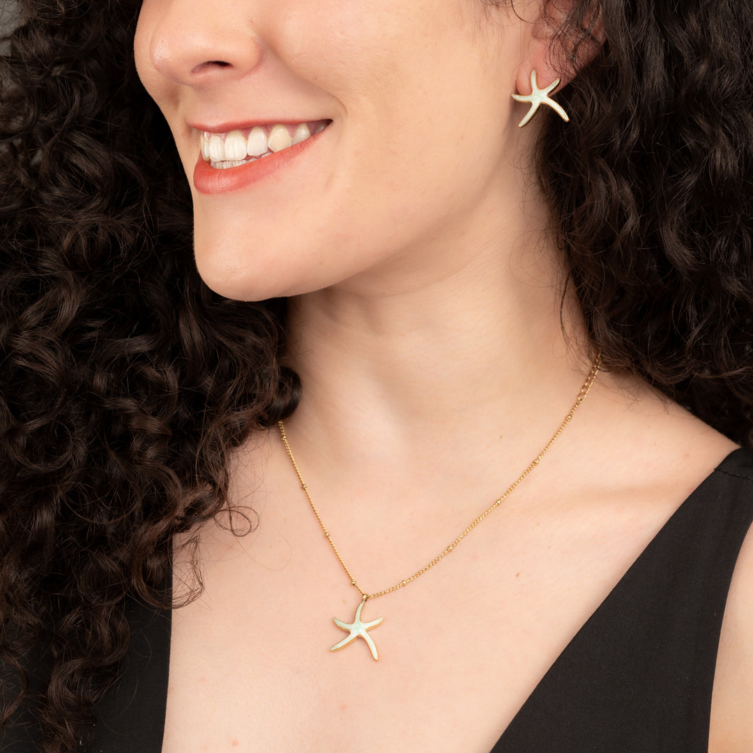 A woman wearing a gold starfish shaped jewellery set, matching starfish necklace and earrings, gold plated jewellery, women's artisan jewellery